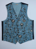A sleeveless vest with a dusty blue base and an all-over floral pattern in brown, gray, and white. It features black side panels and black trim along the neckline and armholes, photographed flat against a light gray background.